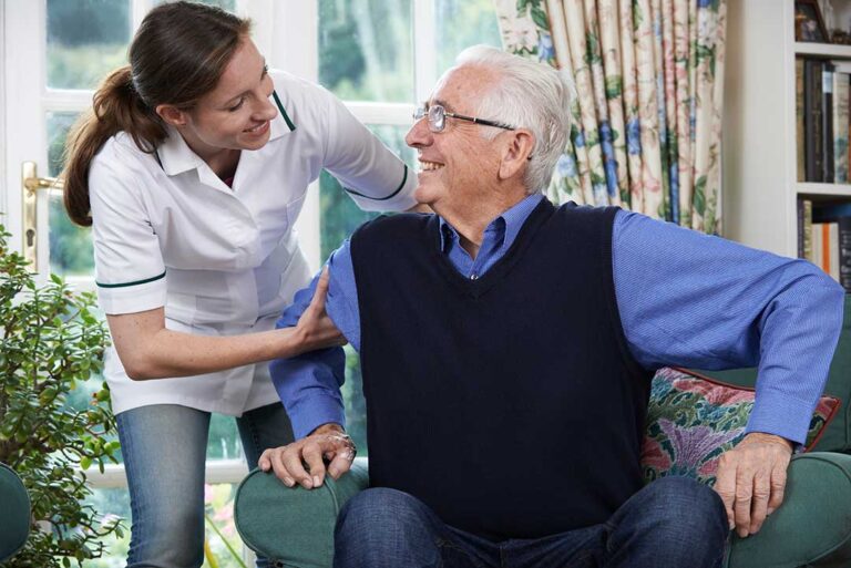 Older adults sharing a quiet conversation at a table in a bright assisted living common room.
